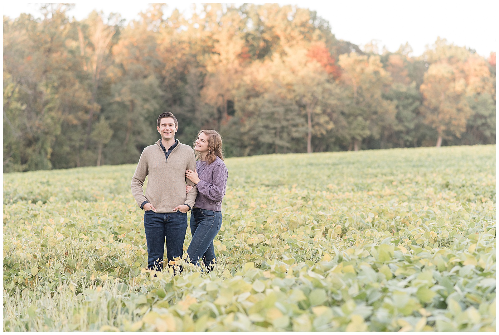 engaged couple standing in field surrounded by plants as girl holds onto guy's left arm and looks up at him at elizabeth furnace in lititz pennsylvania