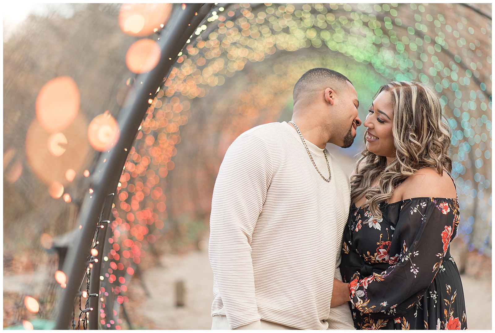 engaged couple smiling and almost kissing under archway filled with colorful lights at longwood gardens