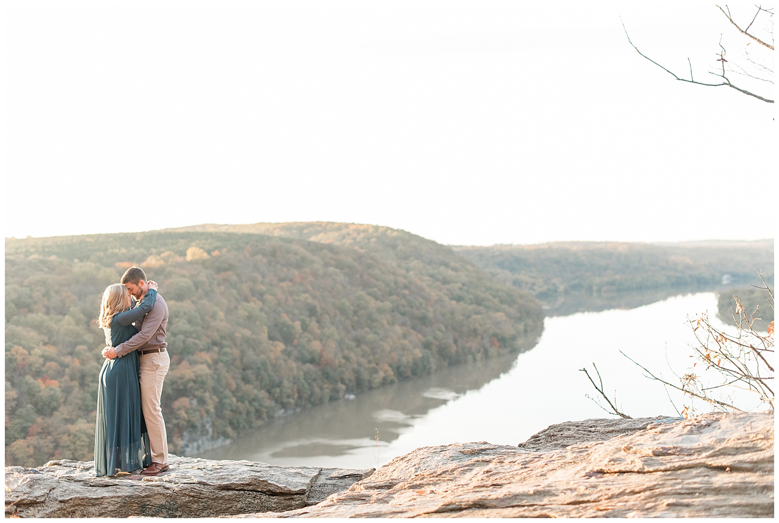 engaged couple hugging tightly almost kissing atop large rock at pinnacle point overlook on fall day in holtwood pennsylvania