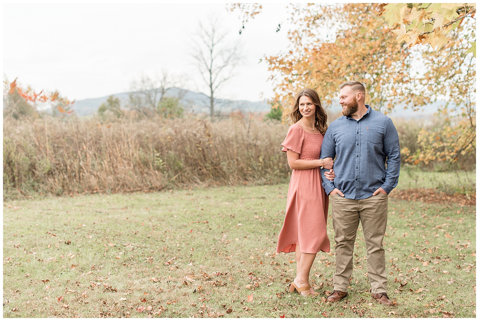 woman wrapping her arms around guy's right arm as he smiles and looks at her near colorful tree and wild grasses in lititz pennsylvania