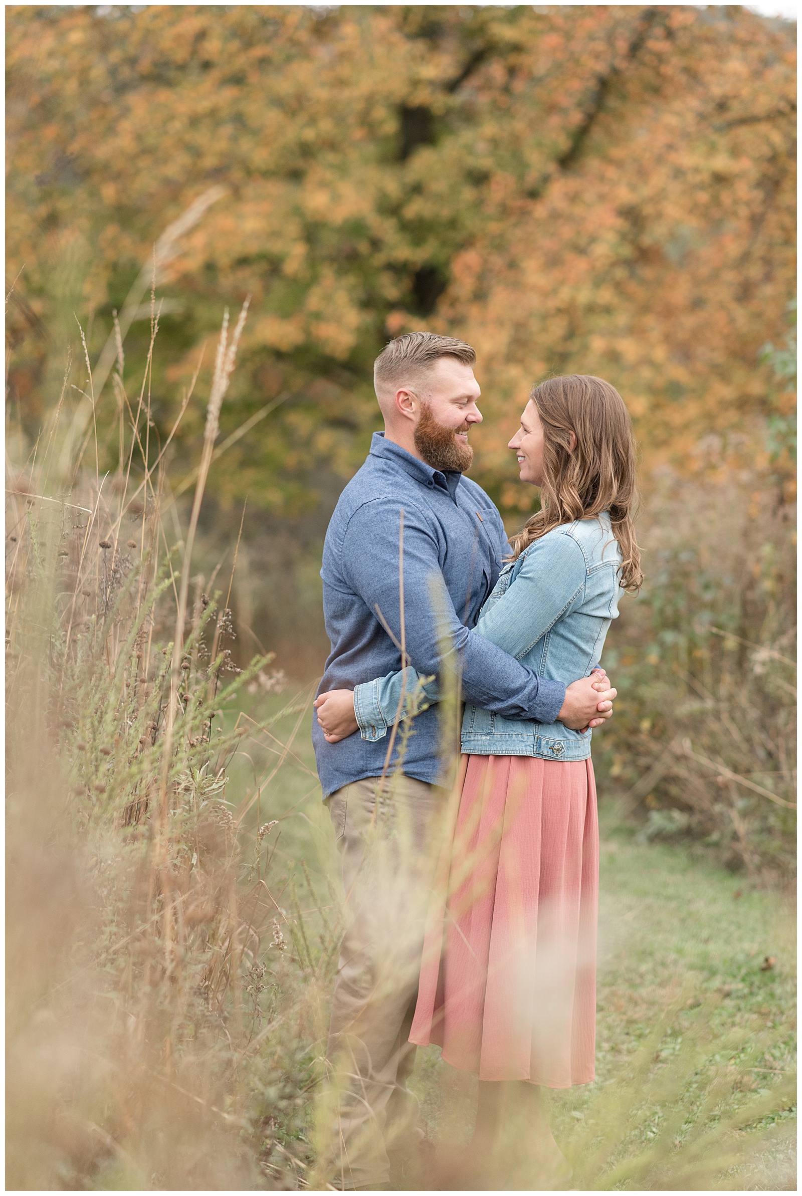 engaged couple hugging tightly as they smile and look at each other by tall wild grasses at middle creek wildlife preserve