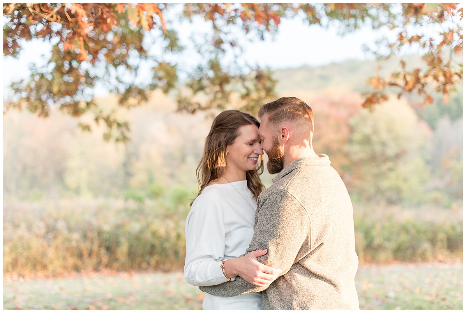 engaged couple smiling with their foreheads touching as they hug on sunny fall day at middle creek wildlife in lititz pennsylvania