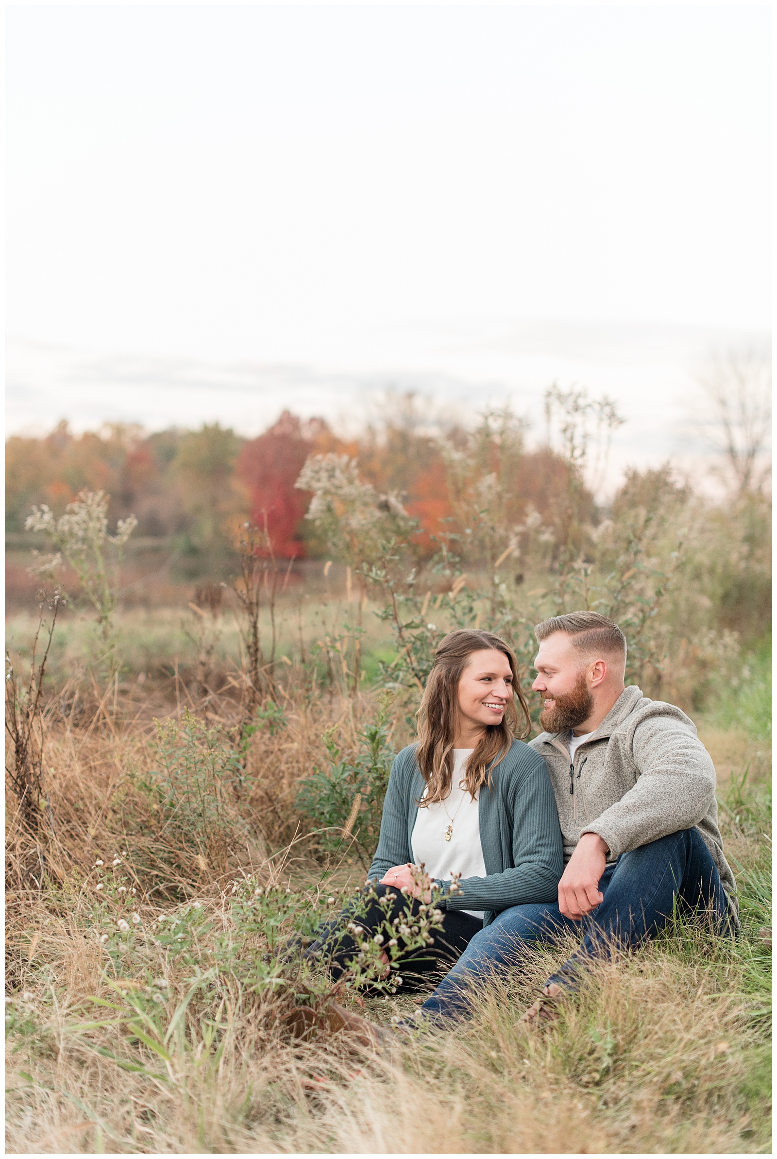 engaged couple sitting close together by colorful fall wild grasses at middle creek wildlife preserve