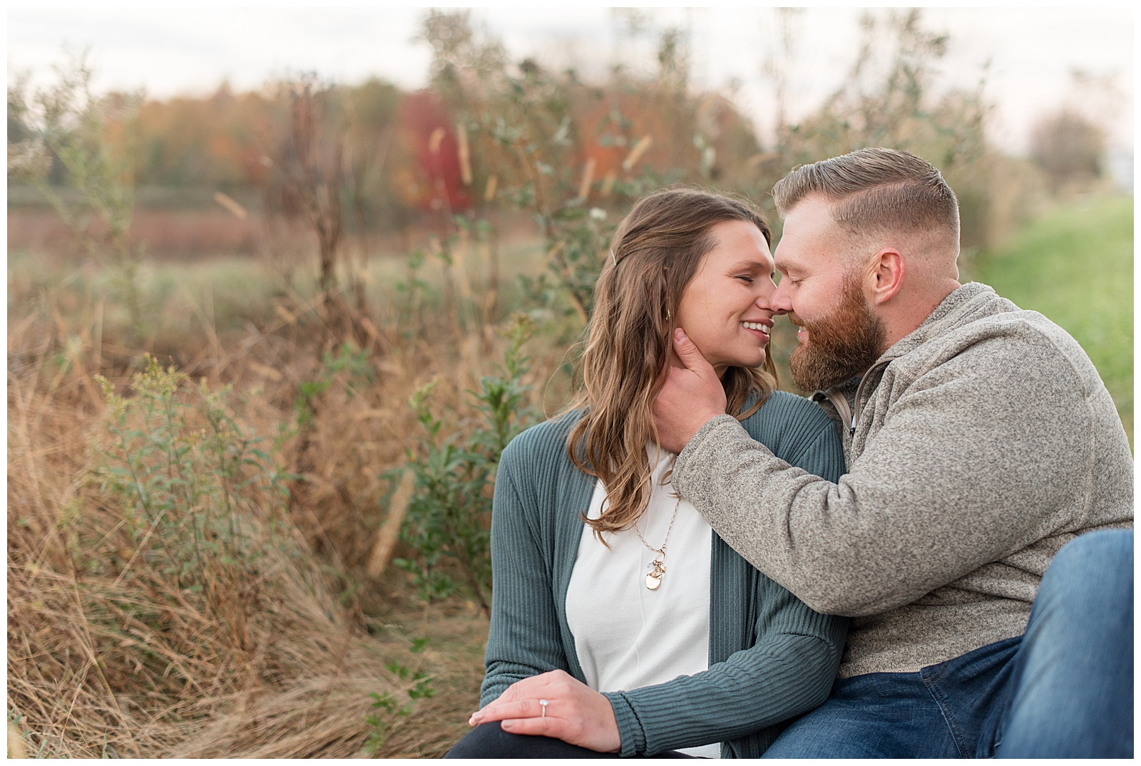 couple almost kissing as they smile and guy holds girl's right jawline sitting by wild grasses at middle creek in lancaster pennsylvania