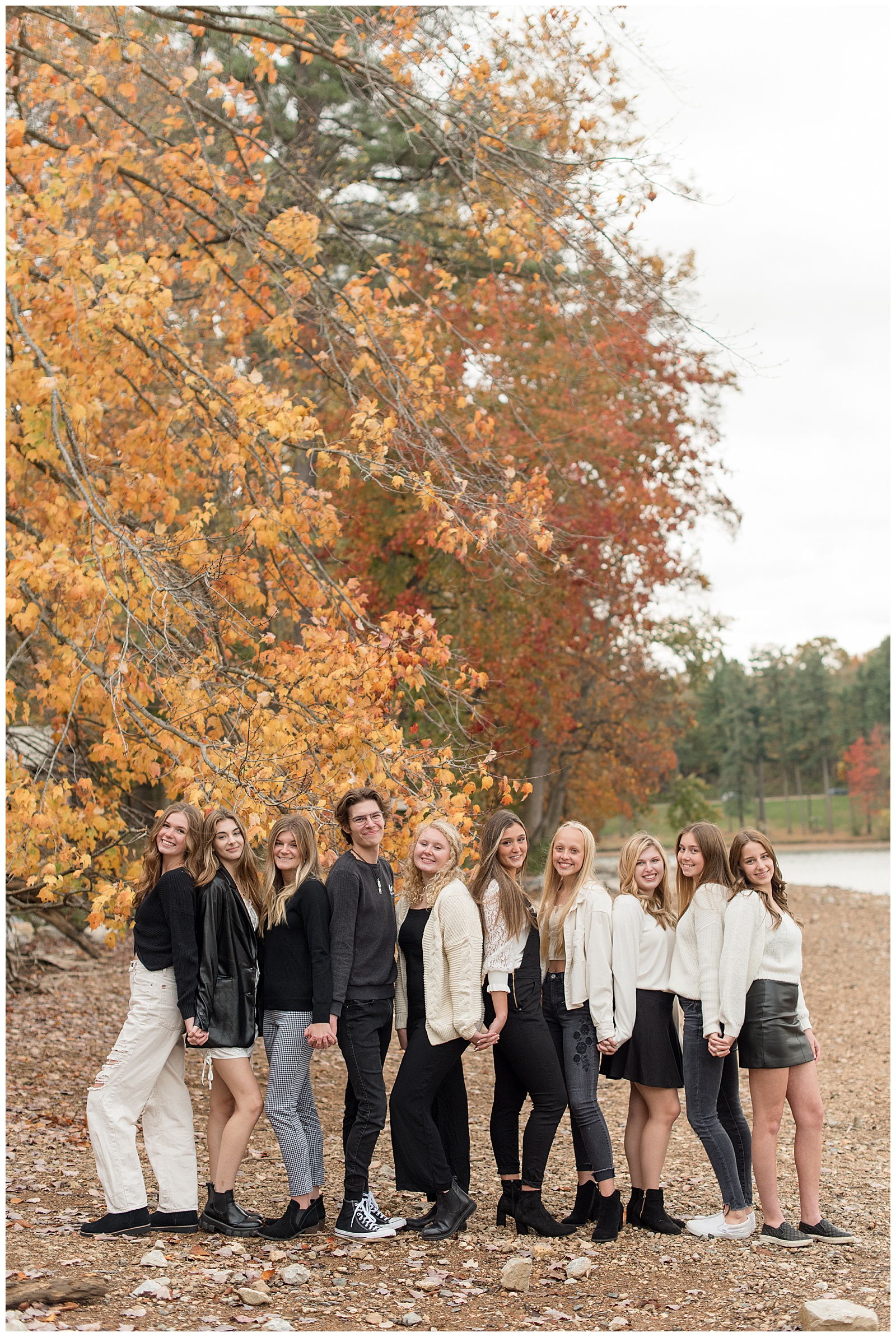 senior spokesmodels standing close together with their backs against one another with fall tree behind them at reservoir park