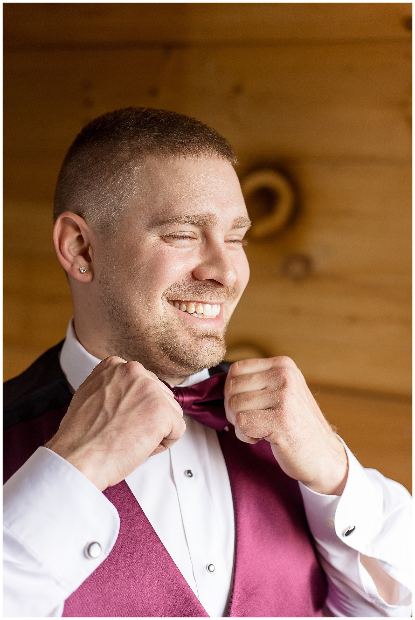 close up photo of groom smiling big as he holds his maroon bowtie at walnut grove farms