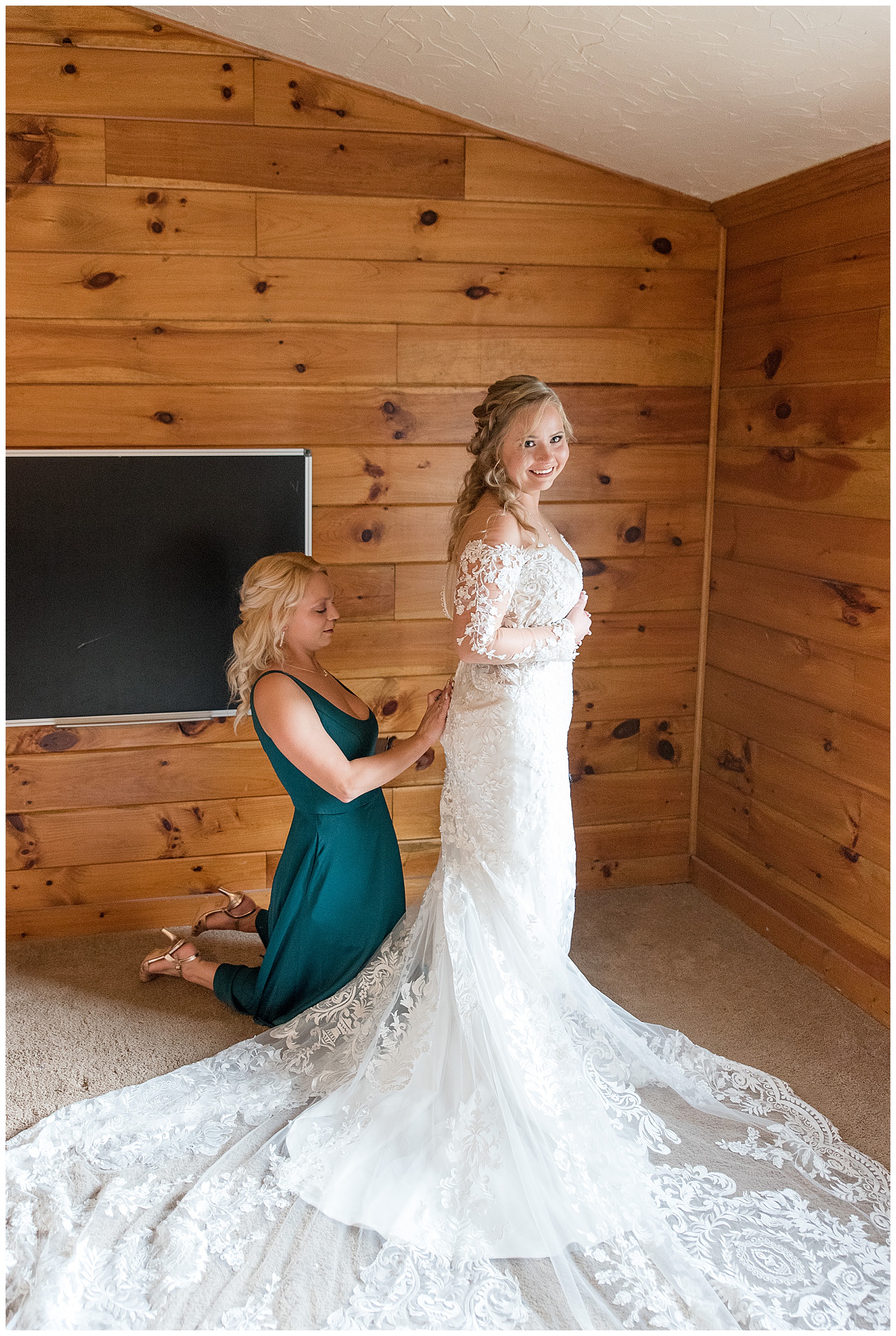 matron of honor in dark teal gown buttoning up the bride's back of her white gown in bridal suite in dover pennsylvania