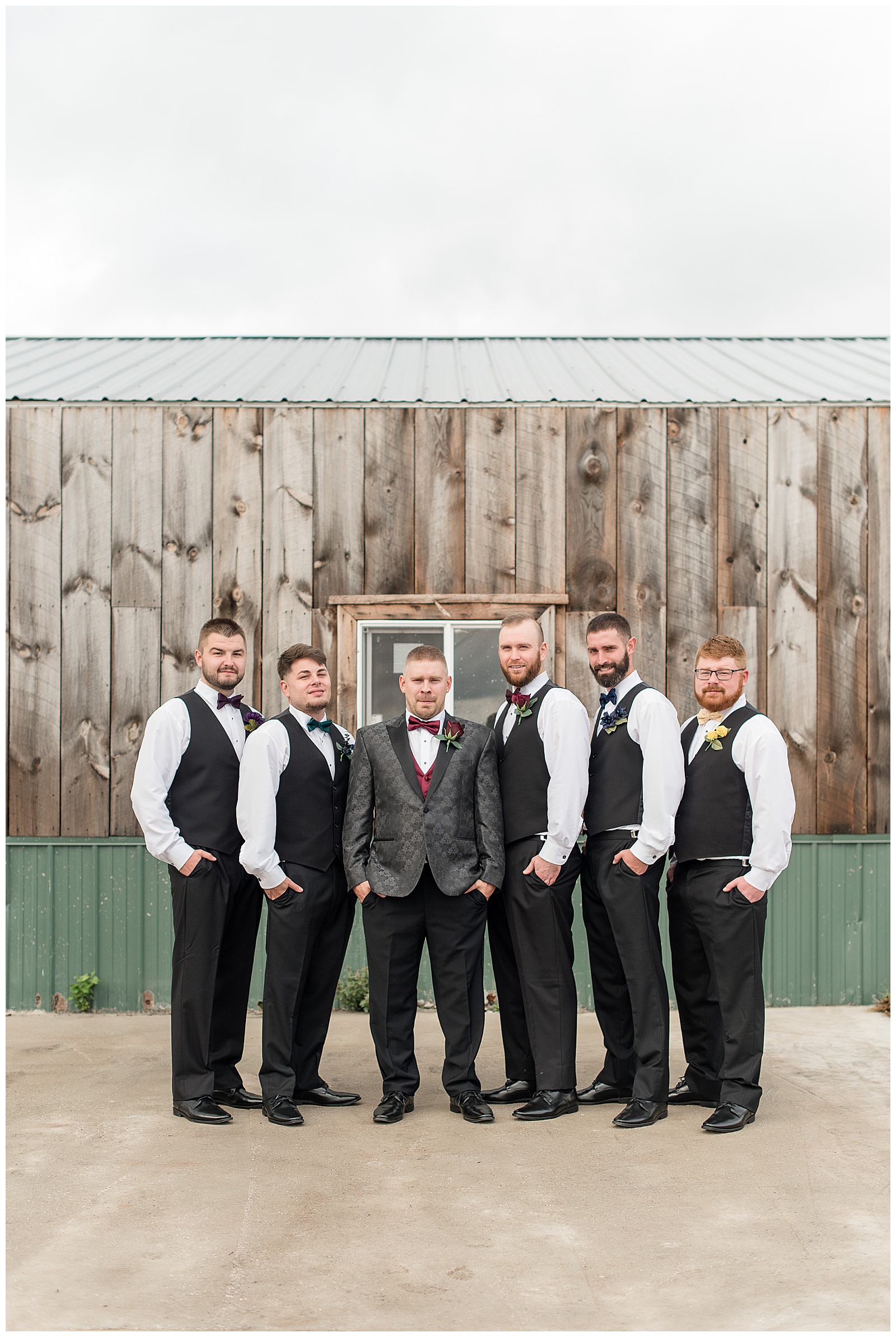 groom surrounded by his five groomsmen all wearing black pants, black vests, white shirts, and maroon bowties at walnut grove farms