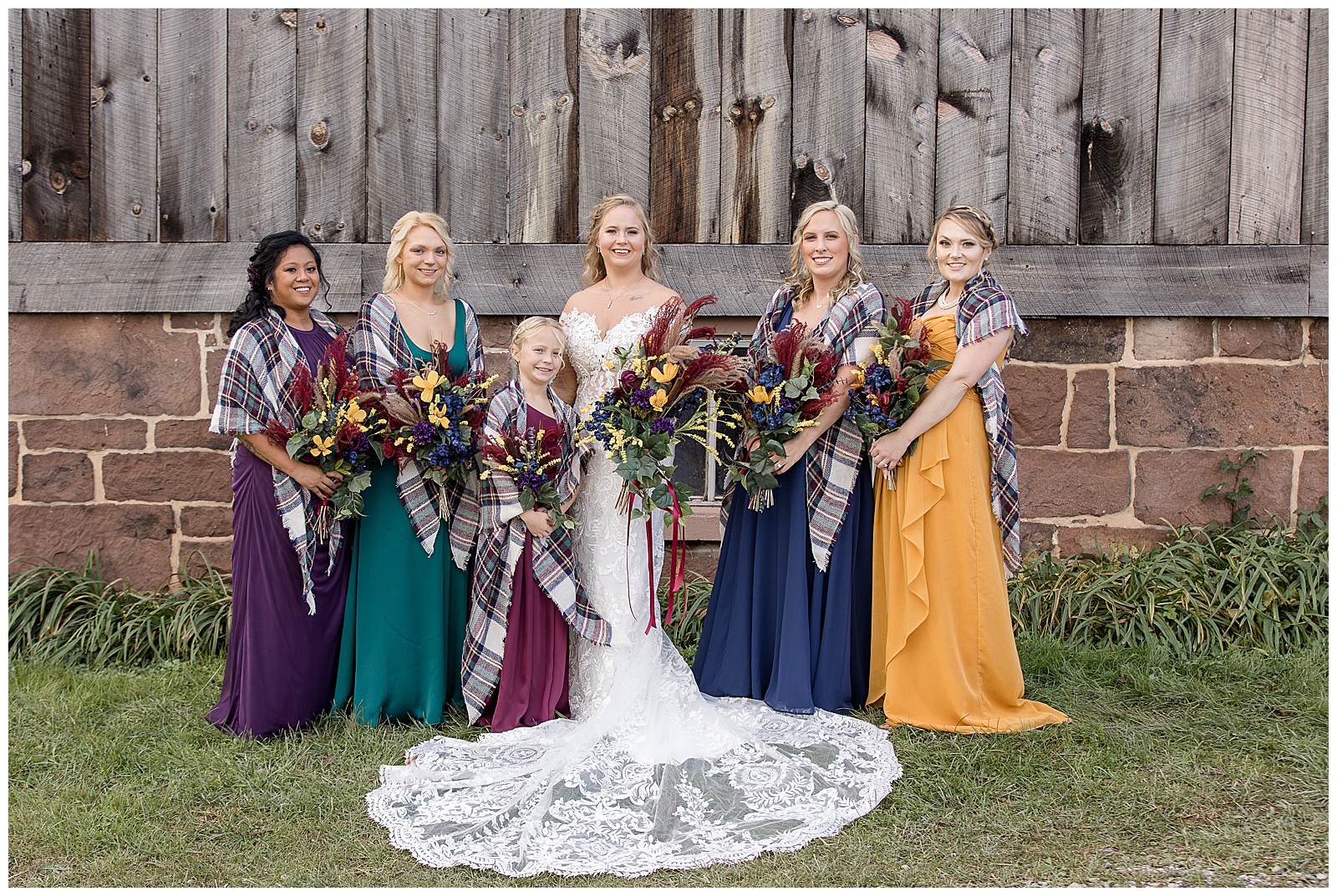 bride with her daughter and four bridesmaids all wearing different fall colored dresses by rustic barn at walnut grove farms