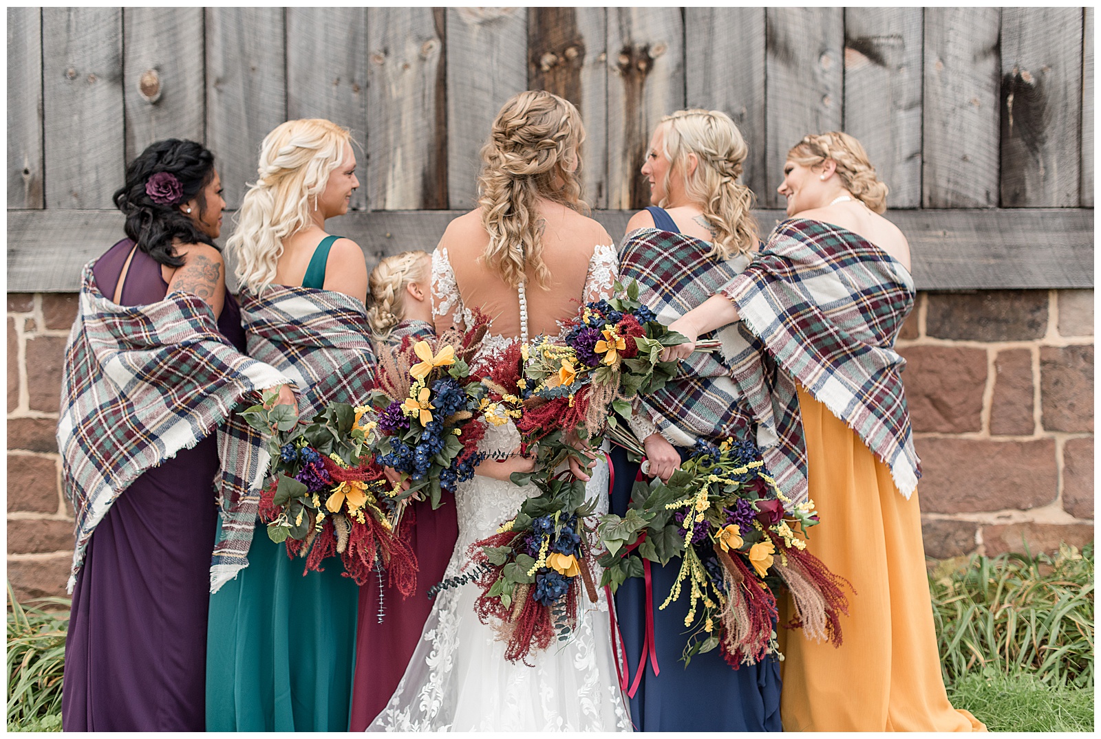 backs of bride and her bridesmaids toward camera with their flower bouquets displayed near rustic barn in dover pennsylvania