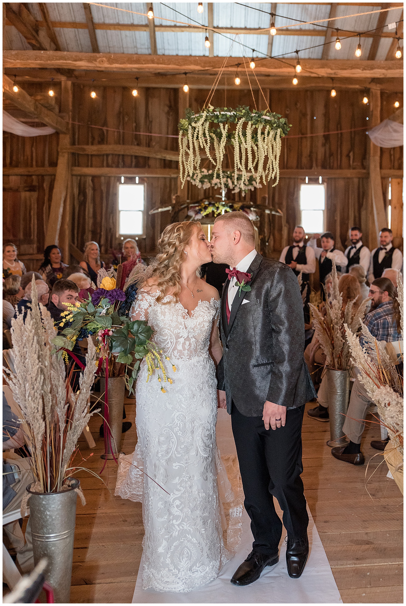 bride and groom share a kiss as they leave their wedding ceremony and guests smile and watch behind them at walnut grove farms