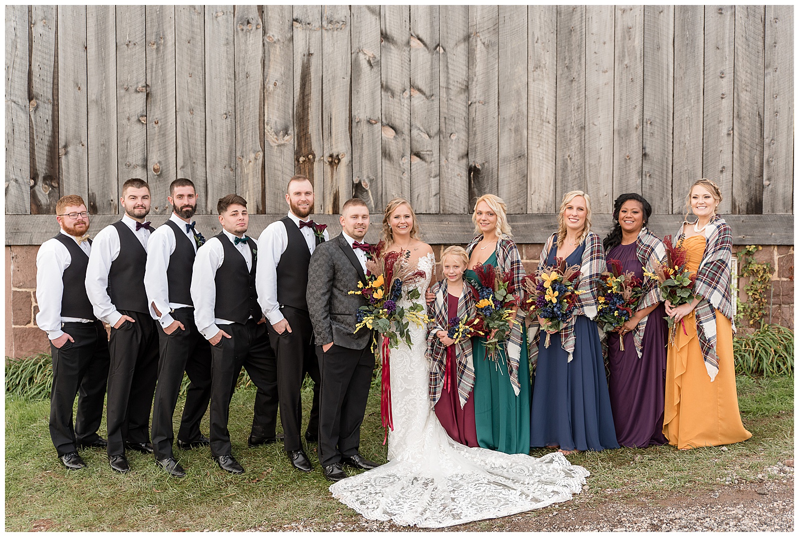 bride and groom surrounded by their colorful wedding party by rustic gray barn at walnut grove farms
