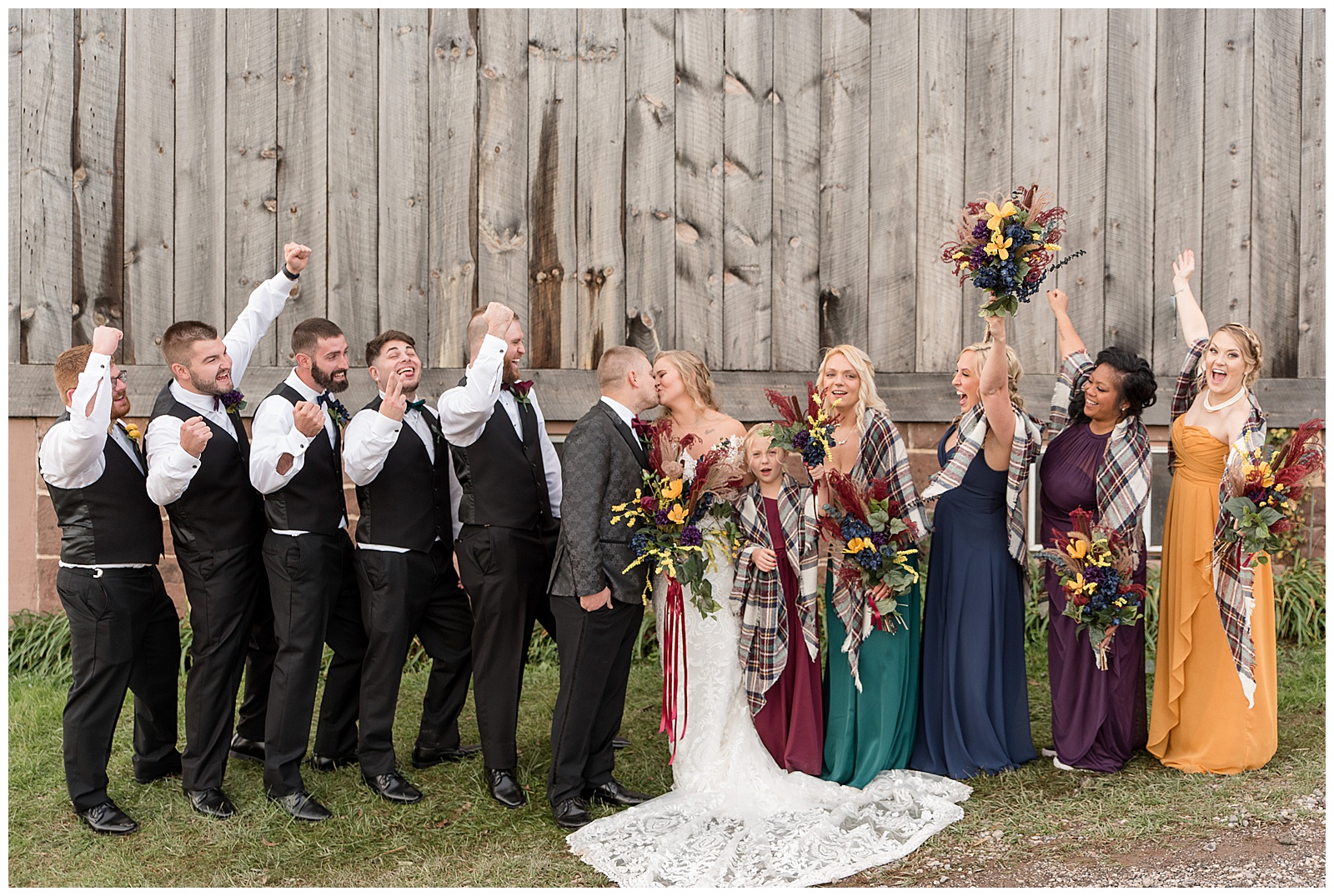 bride and groom kissing as their bridal party cheers them on and smiles by rustic gray barn in dover pennsylvania