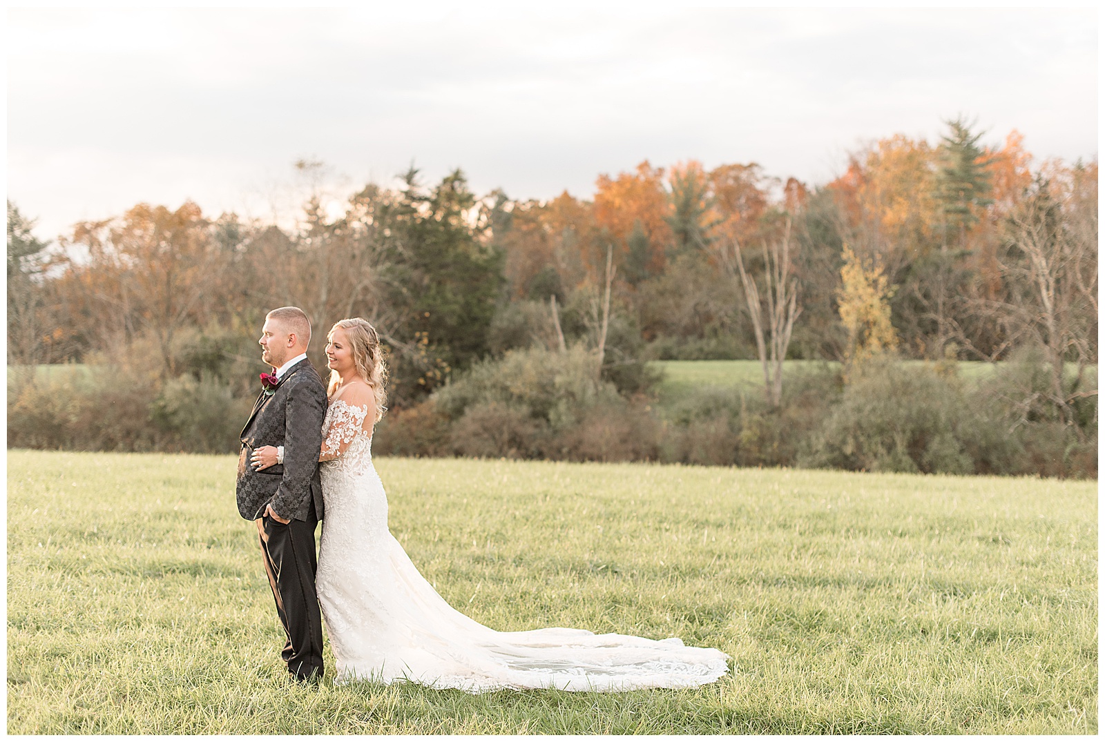 groom facing the right with bride hugging him from behind with her dress displayed behind her on grass field at walnut grove farms