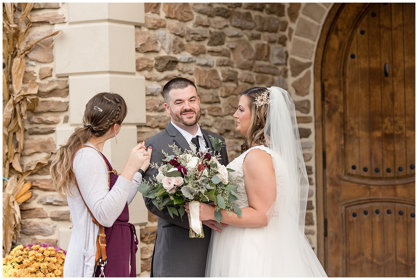 photographer holding her camera as she chats with groom and bride as they stand by stone wall at folino estate