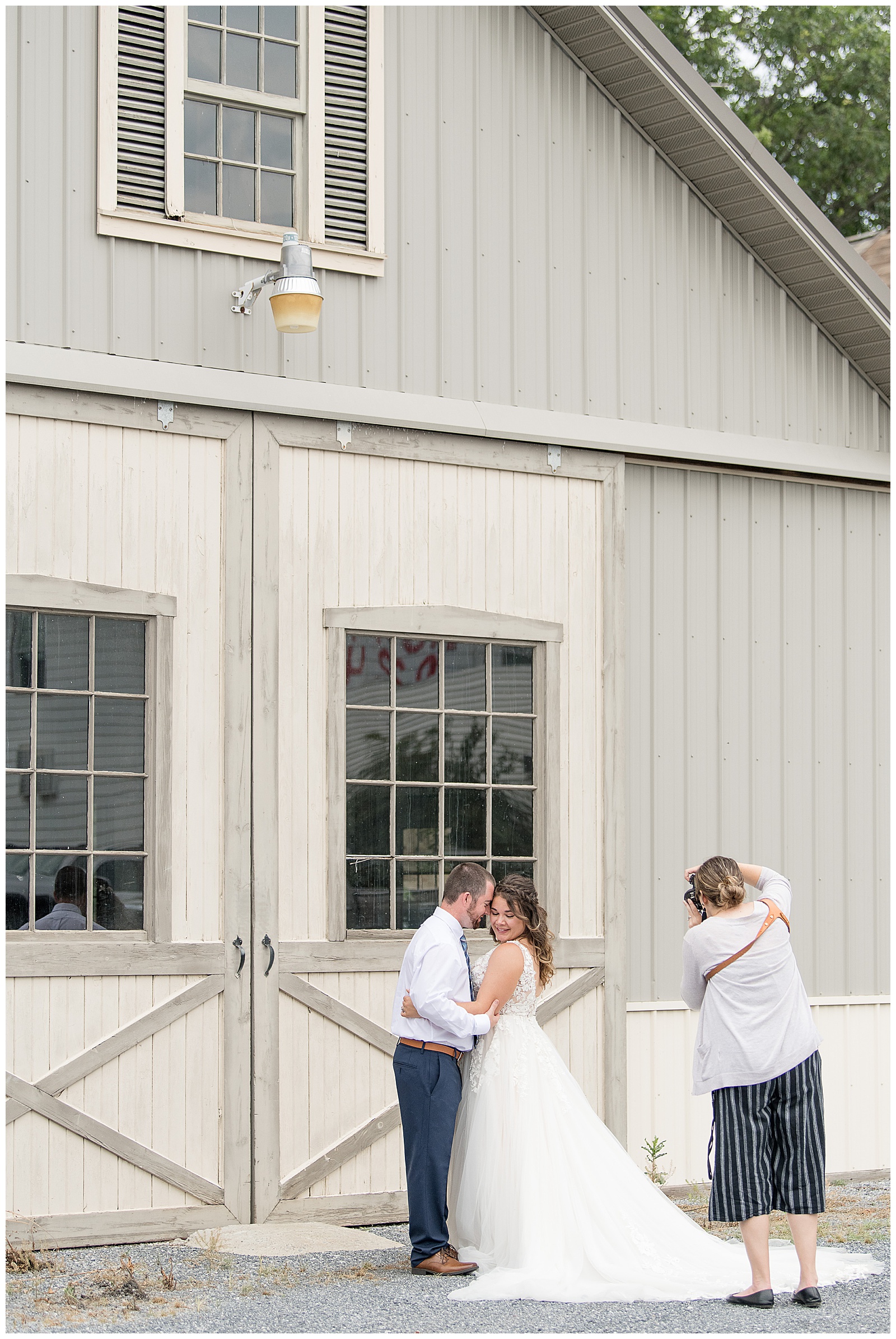 photographer taking photos of groom and bride hugging by large tan barn doors at the silk mill on main in new holland pennsylvania