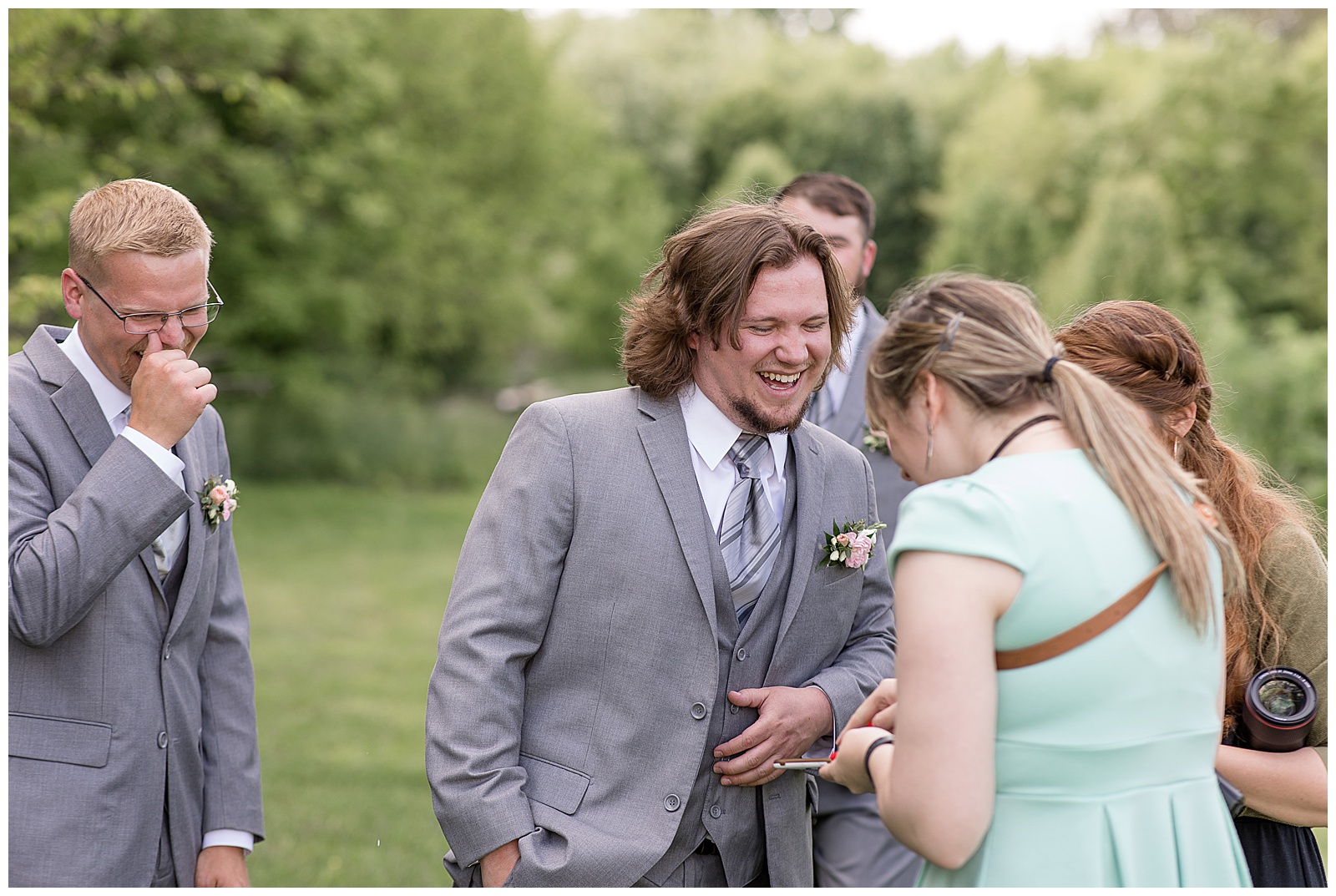 back of photographer towards camera as she's holding something small in her hand and groomsman and groom are laughing hysterically in lancaster pennsylvania