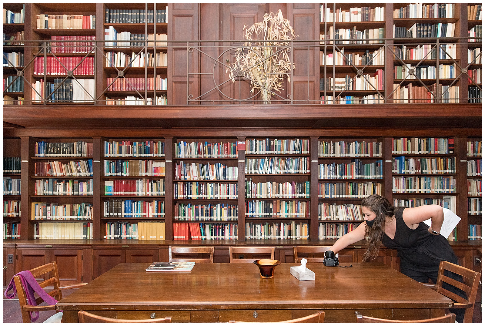 photographer leaning across large wooden table inside library as she arranges objects on table on wedding day