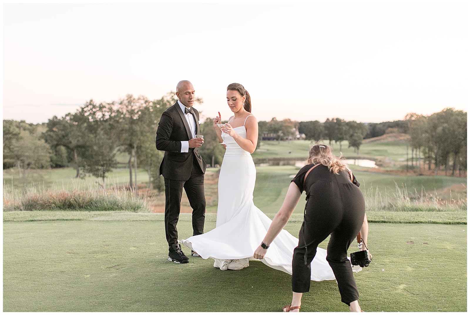 couple standing on golf green and chatting as photographer arranges bride's dress train perfectly at north jersey country club