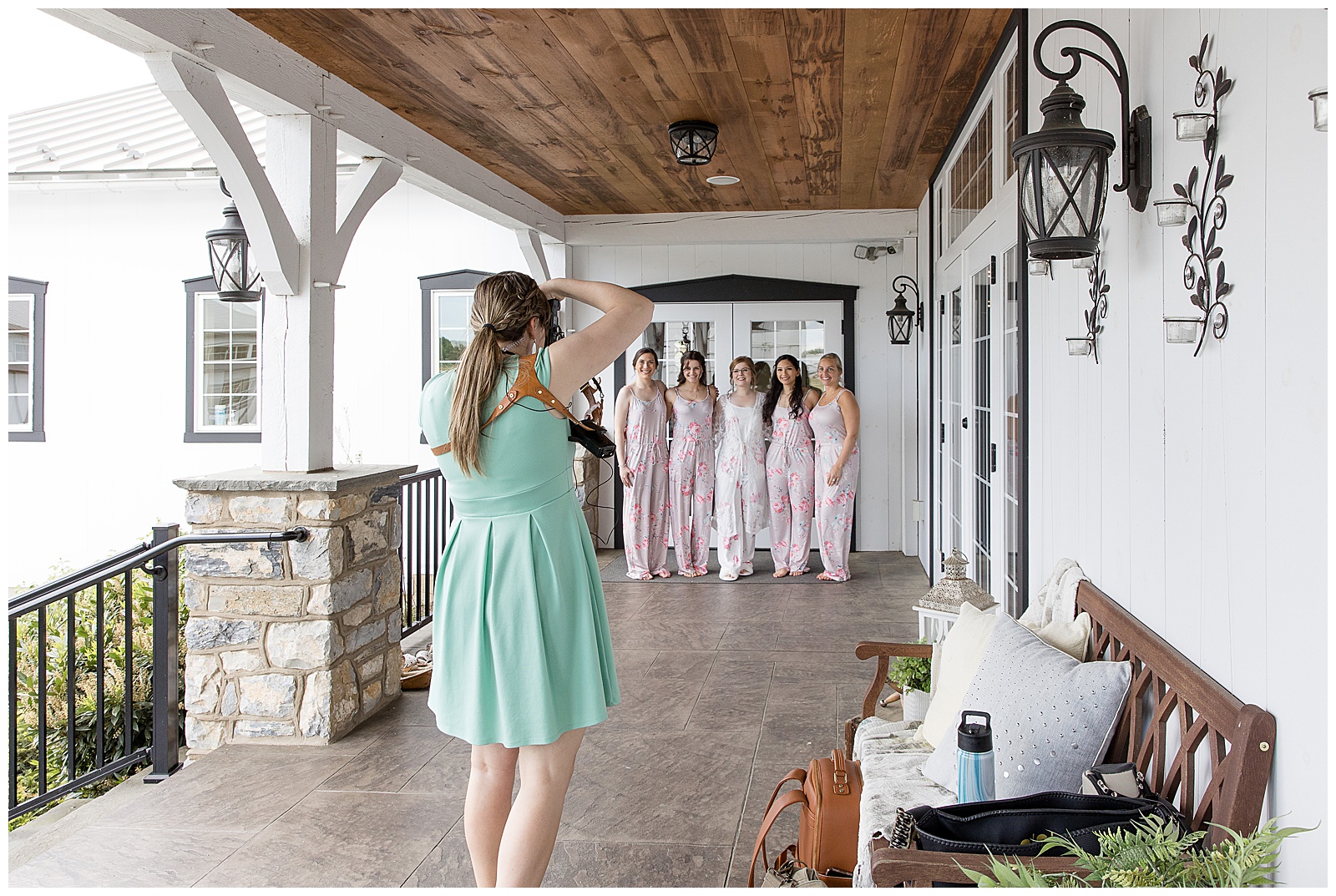 back of photographer as she snaps photos of bride and bridesmaids under wooden porch on wedding day