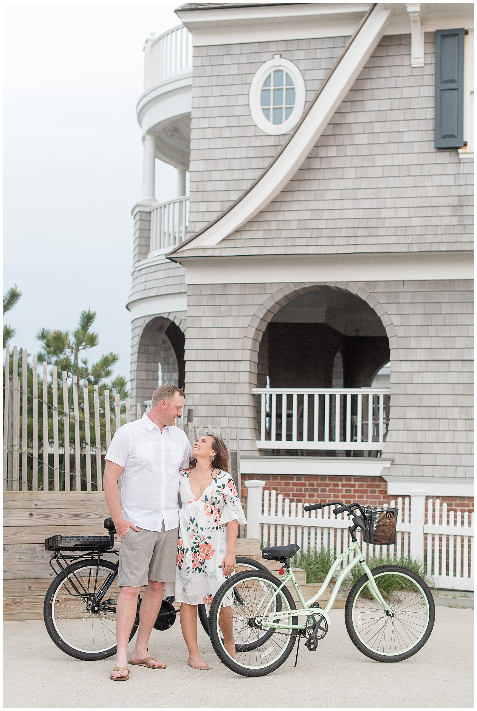 engaged couple hugging and looking at each other smiling beside two bikes along sidewalk by beach house in new jersey