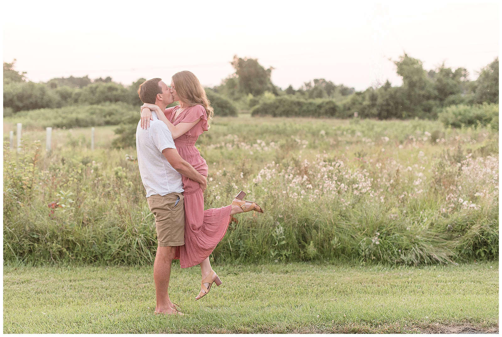 engaged couple kissing as man lifts woman off the ground and she kicks up her left foot by beautiful wildflower field in lancaster pennsylvania