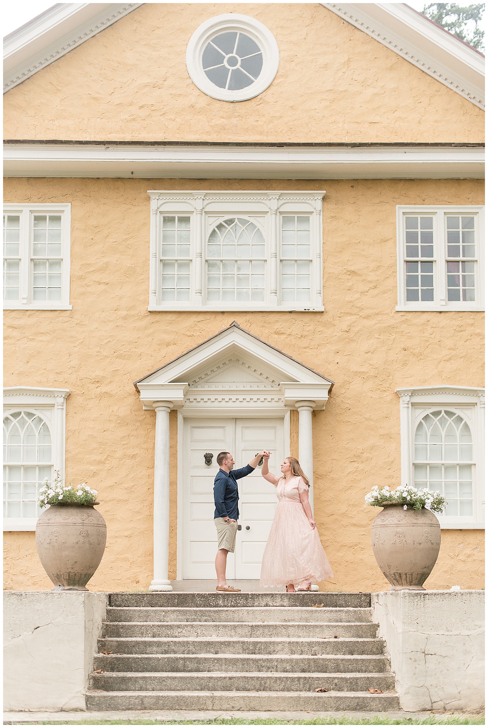 man twirling woman under his left arm as she holds out long dress with her left hand atop concrete steps in front of stately peach and white home in pennsylvania