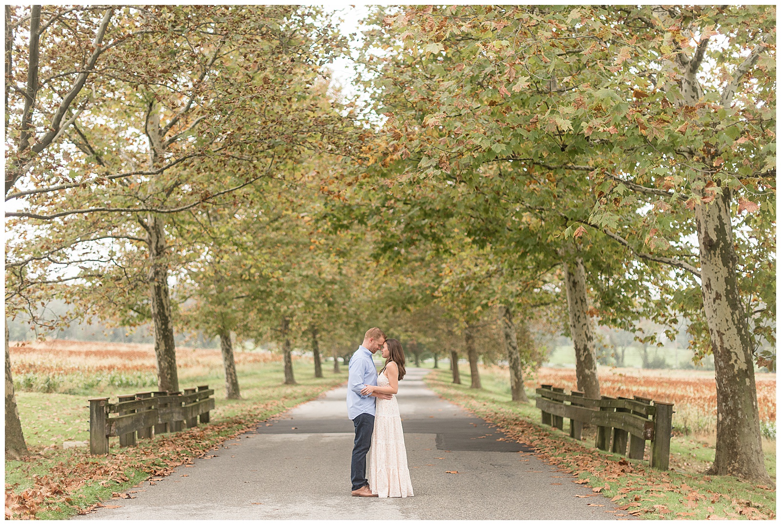 engaged couple hugging and almost kissing in middle of paved tree-lined pathway at farm in pennsylvania on fall day