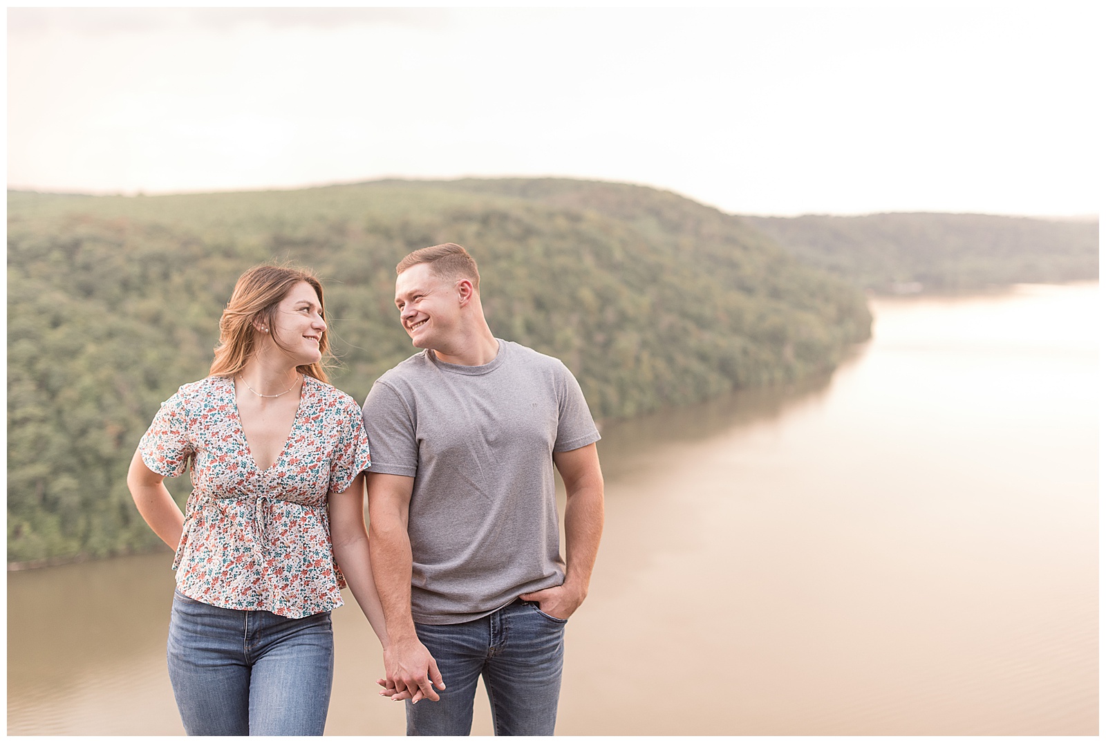 engaged couple holding hands and smiling as they look into each others' eyes atop pinnacle point overlook above susquehanna river in holtwood pennsylvania