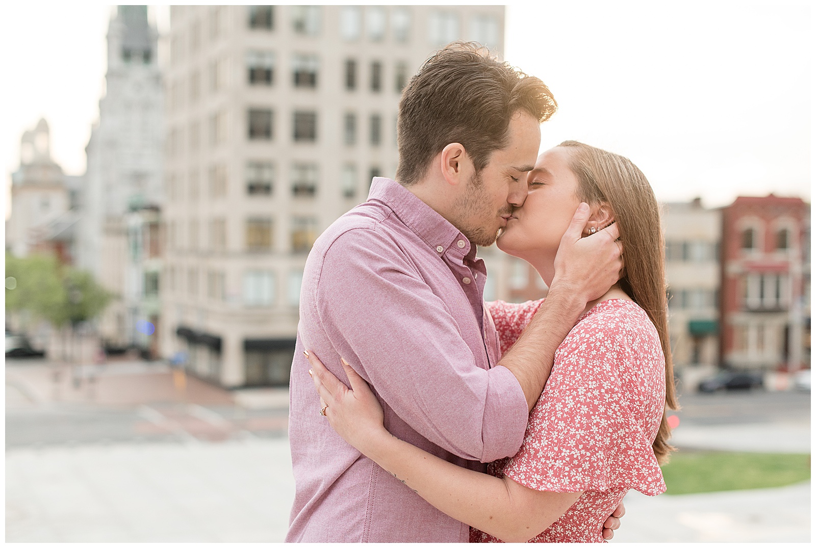 engaged couple kissing in downtown harrisburg on sidewalk with large building behind them on sunny evening in pennsylvania
