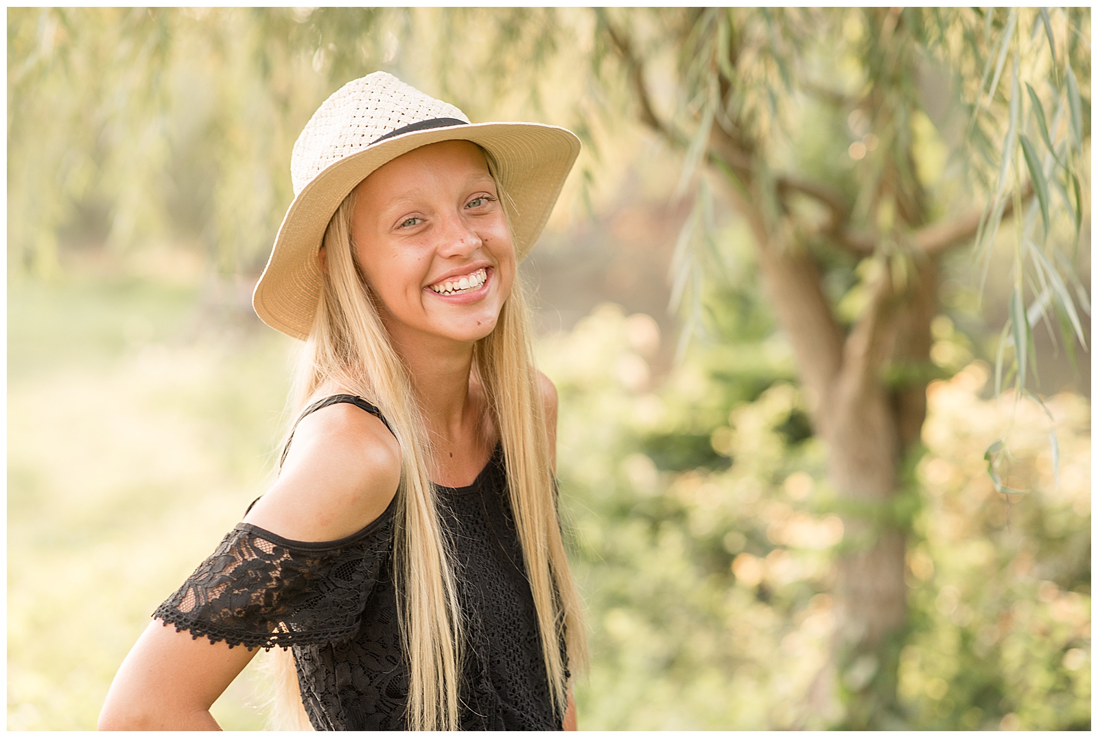 senior girl wearing trendy tan and black hat with black tank top standing by tree on bright summer evening and smiling at camera in southeastern pennsylvania