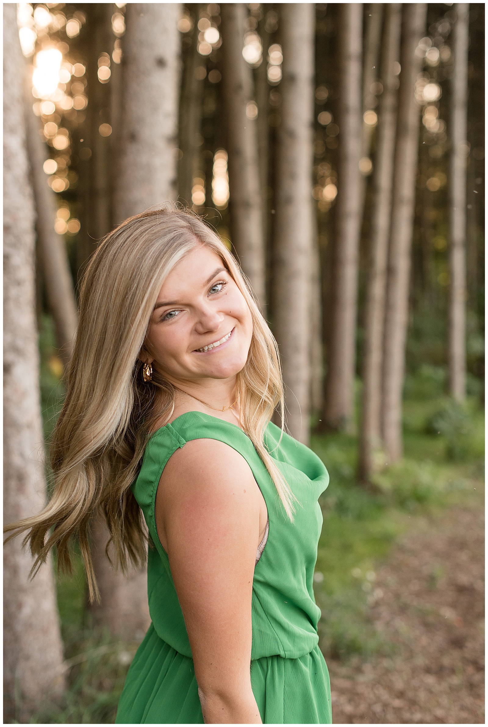 senior girl with right shoulder towards camera wearing green dress and smiling with hair flowing behind her at overlook park in lancaster pennsylvania