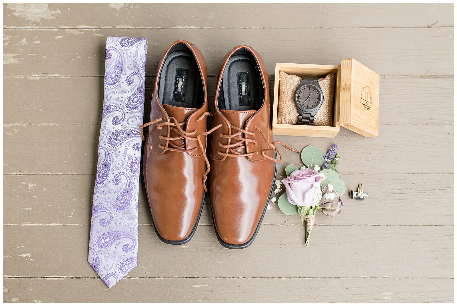 groom's light brown dress shoes on display surrounded by light purple tie, charcoal gray watch inside box, and rose and eucalyptus boutonnerie