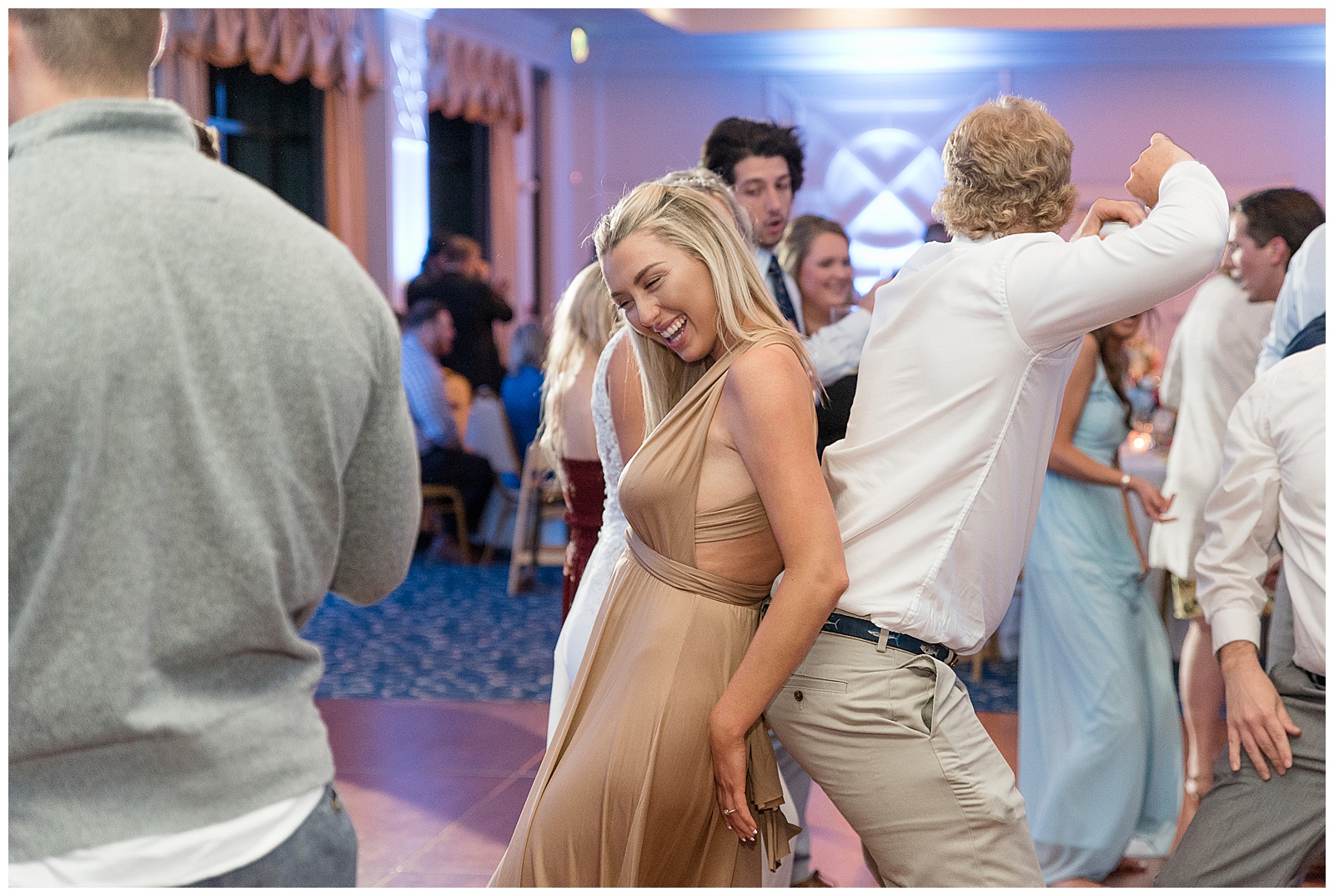 guests dancing with their backs toward one another during indoor wedding reception with colorful lighting in background