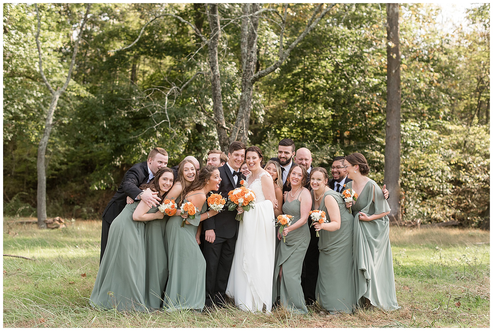 bride and groom surrounded by their bridal party as they all huddle together smiling and leaning in with trees behind them