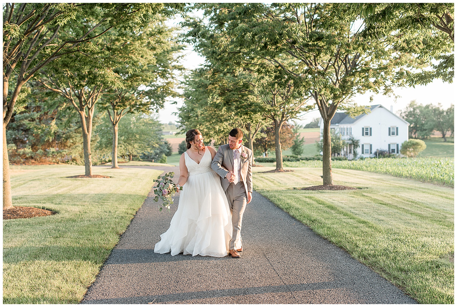 bride and groom walking silly towards camera along paved tree-lined pathway on sunny wedding day