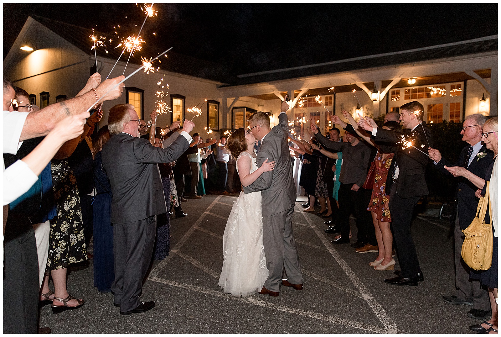 bride and groom kissing outside venue at nighttime surrounded by their guests holding sparklers up high