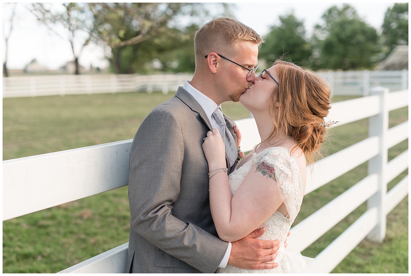 bride and groom standing along white split-rail fence kissing at the barn at silverstone in lancaster pennsylvania