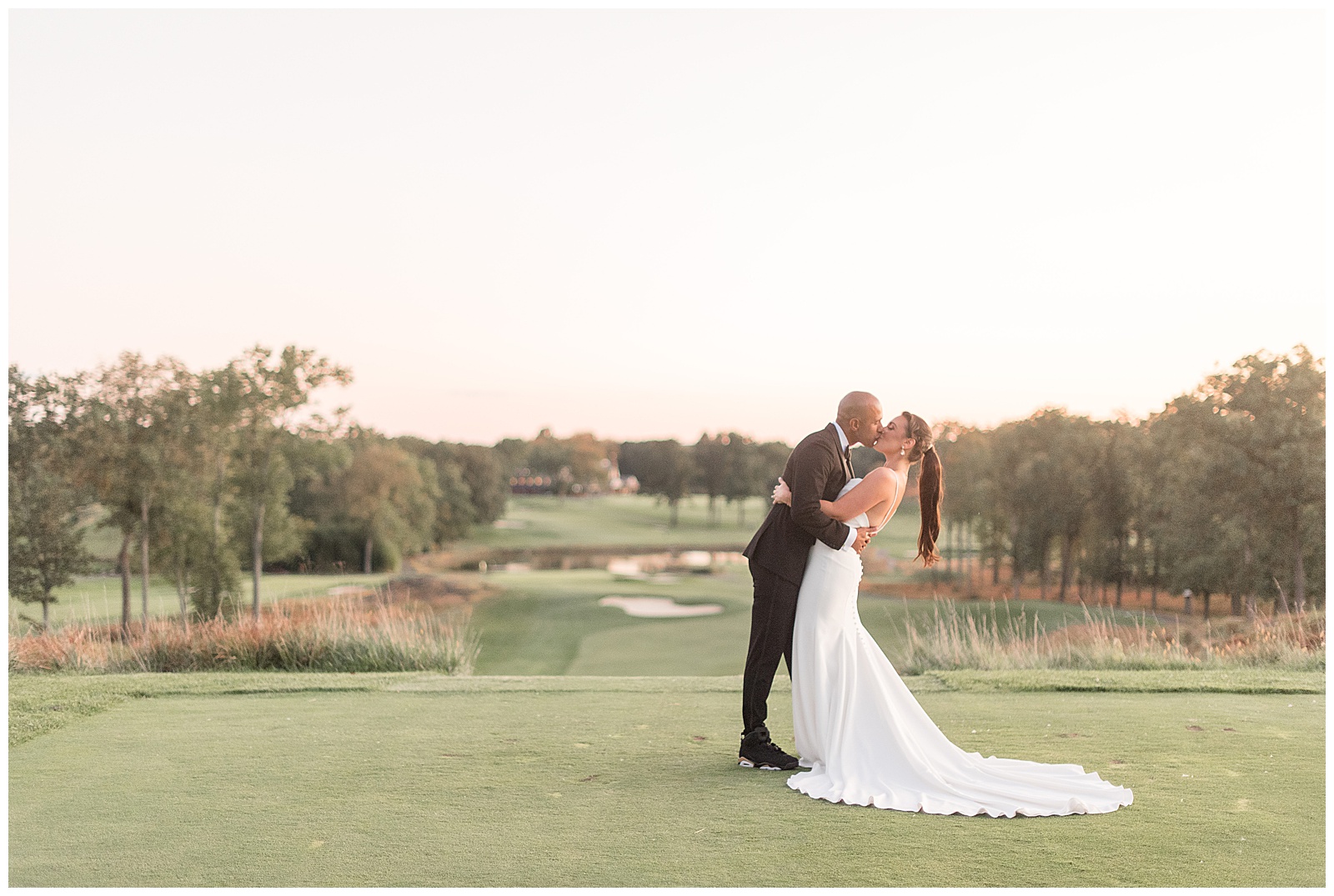 groom slightly dipping his bride back as they kiss standing on golf green at country club in new jersey on sunny day