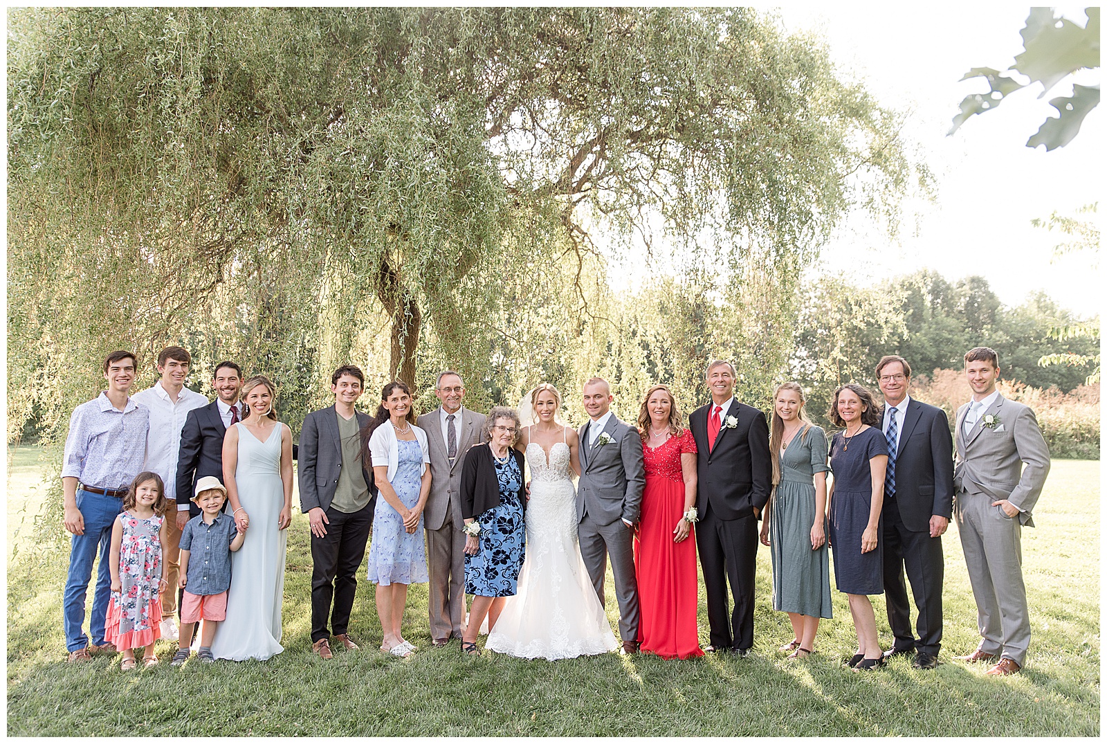 bride and groom surrounded by their families on sunny summer day under willow tree