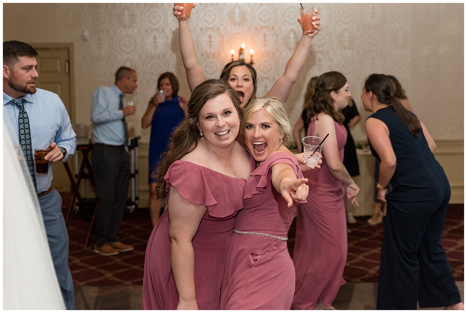 bridesmaids hugging with one pointing at the camera as they smile wearing mauve gowns during reception
