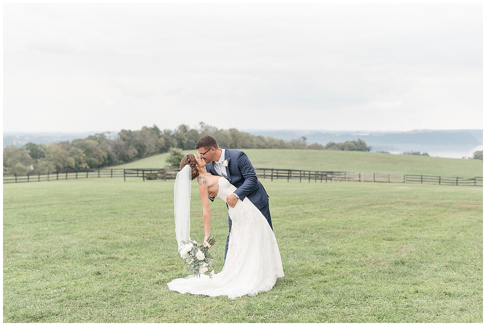 groom dips his bride back as they kiss and she's holding bouquet in her right hand in grassy field at lauxmont farms in pennsylvania