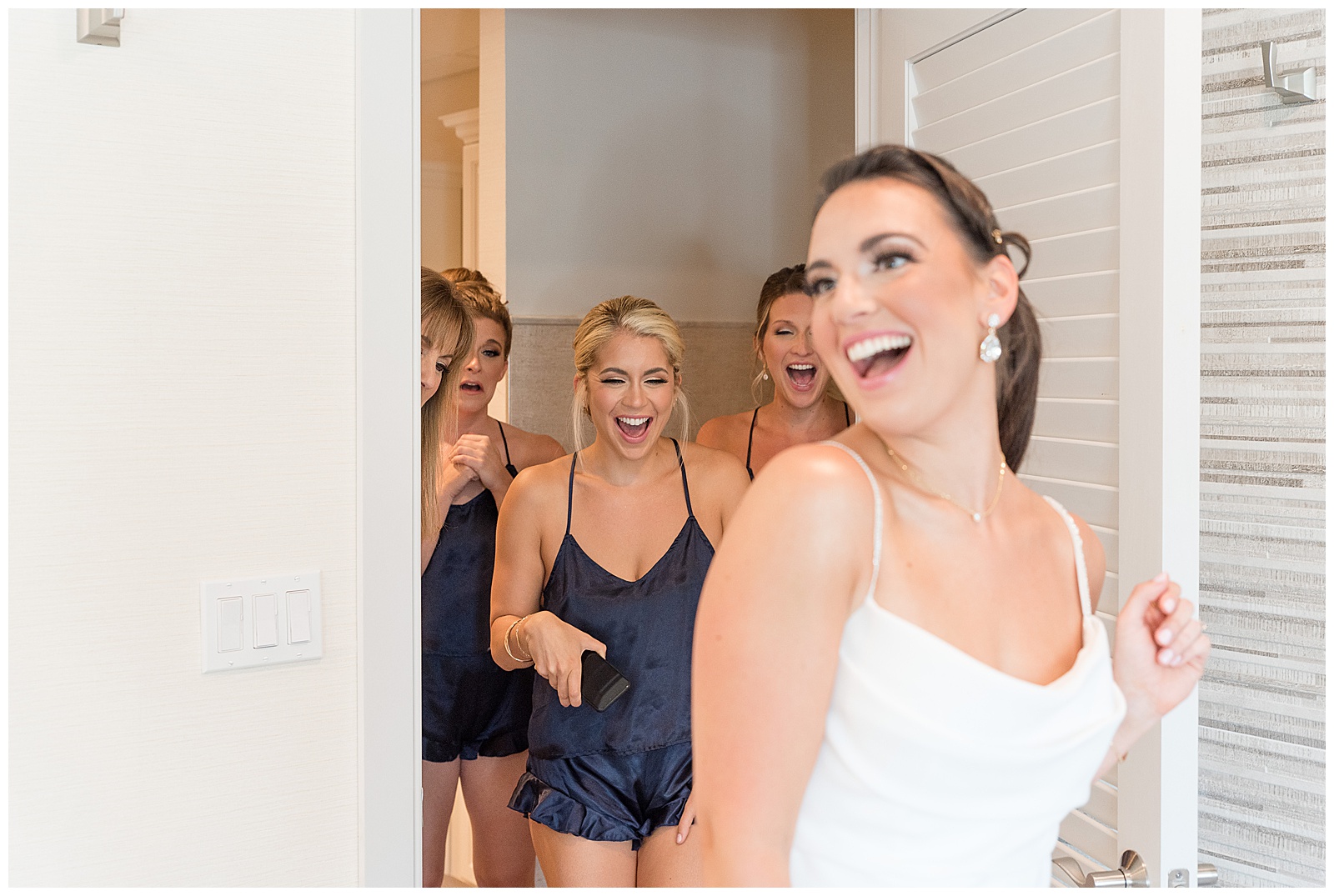 bride looking toward right shoulder with her back towards her bridesmaids as they all smile in bridal suite at country club in new jersey