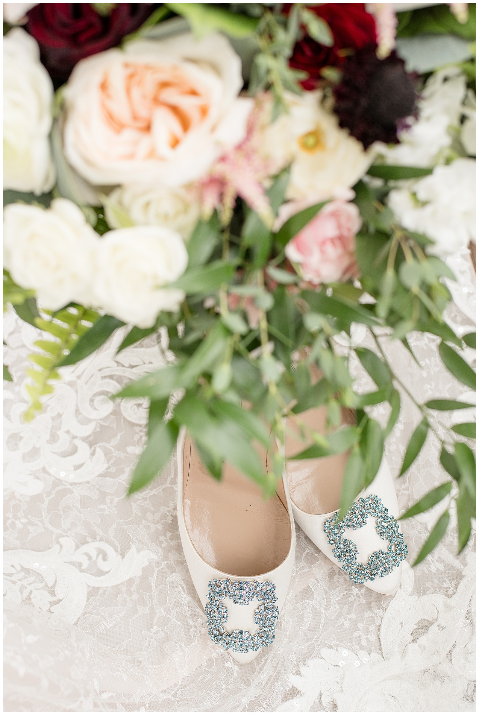 bride's white shoes with blue detailing sitting on lace by beautiful pink and white bridal bouquet