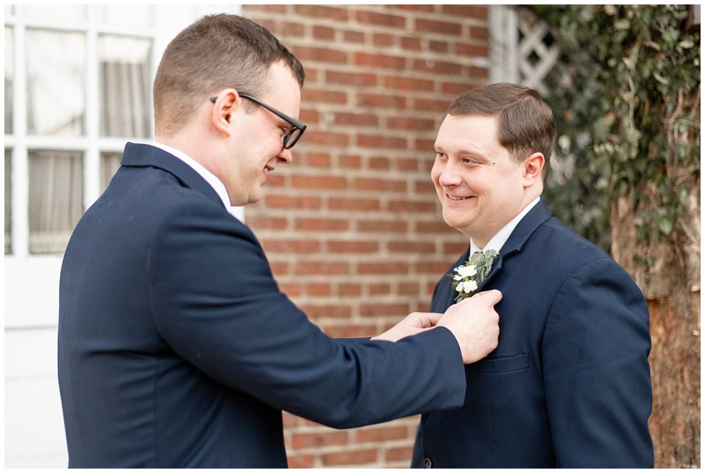 best man helping to pin boutonniere onto groom's suit coat outside brick building in downtown lititz