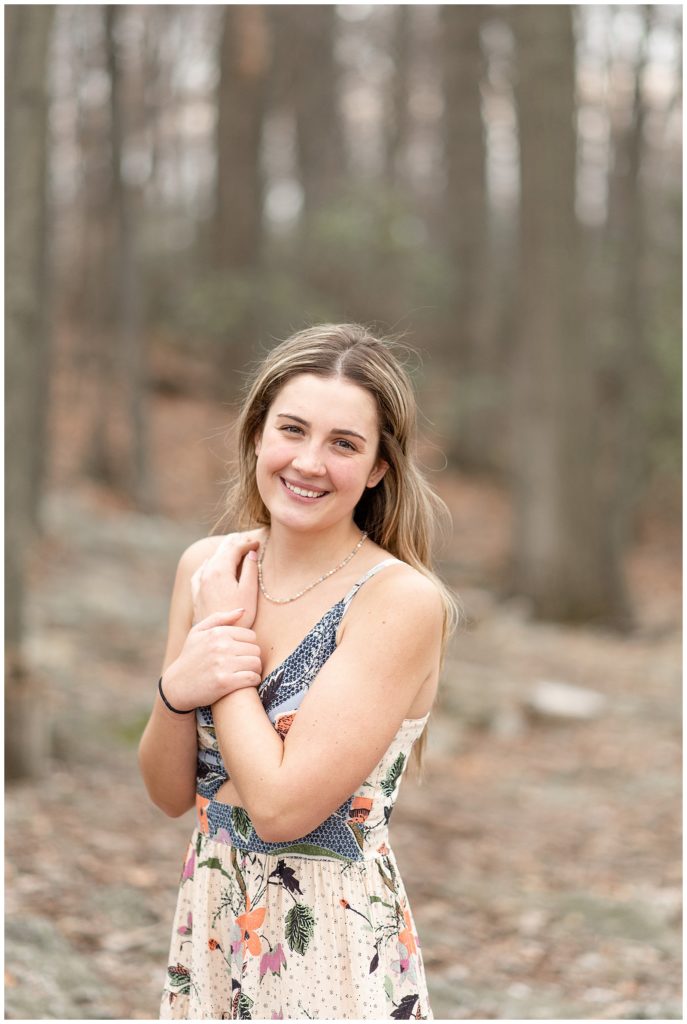 senior girl smiling at camera with hands crossed on chest by woods at samuel lewis state park