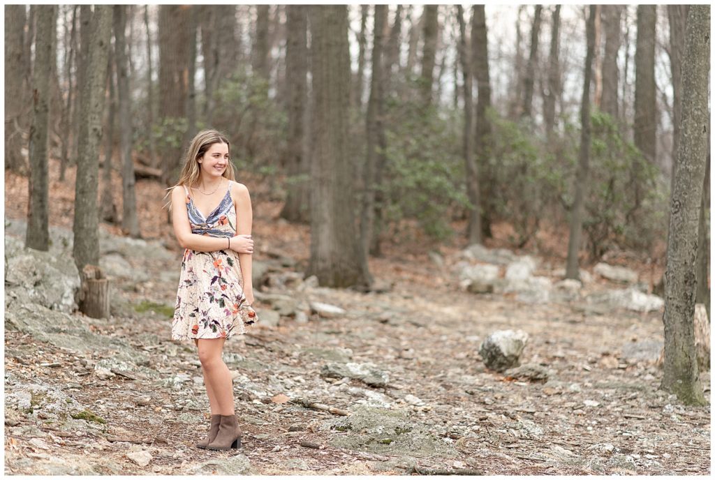 senior girl holding onto left elbow with right hand and looking left by bare trees in york pennsylvania