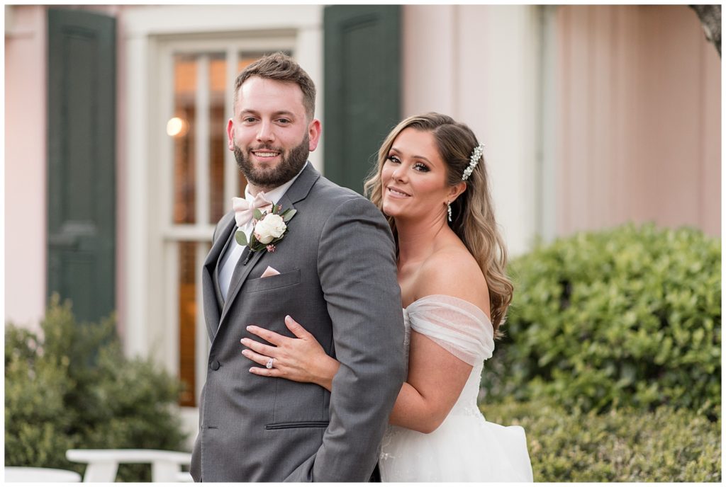 bride hugging her groom from behind as they both smile at camera outside the inn at leola village
