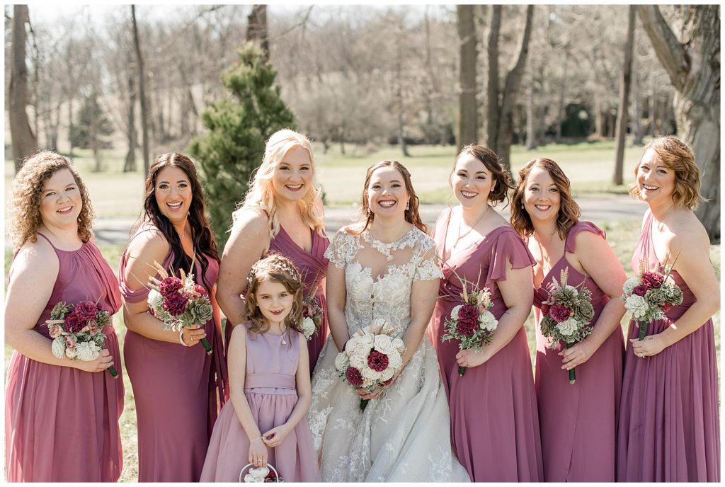 bride wearing lacy wedding gown surrounded by her bridesmaids and flower girl wearing mauve gowns at stock's manor