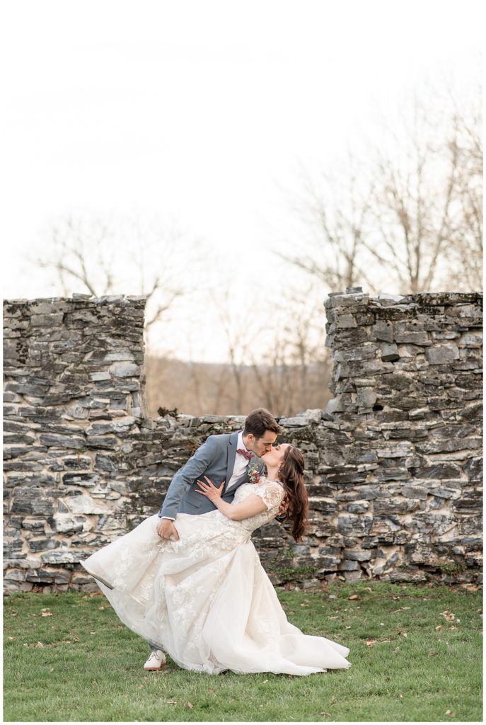 groom dips his bride back as they kiss in front of old stone wall at stock's manor